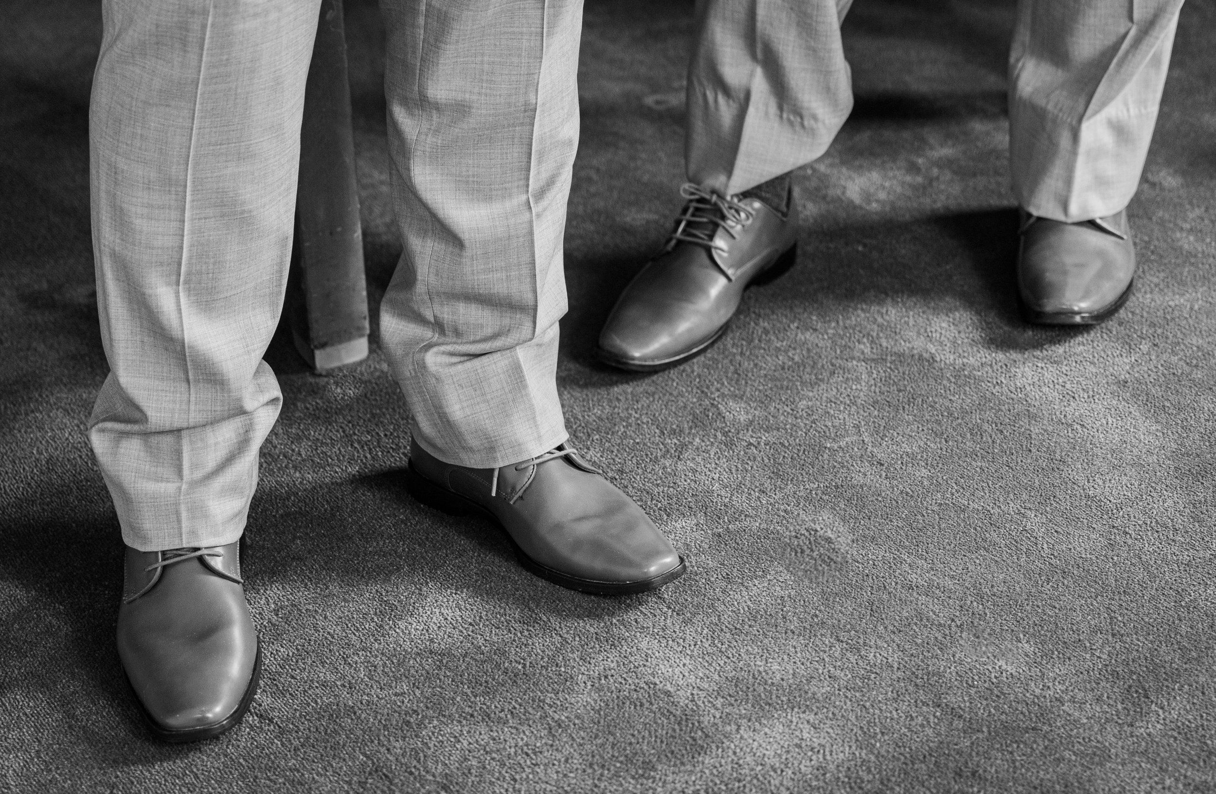 Two people standing close together, dressed in formal pants and shoes on a textured carpet.