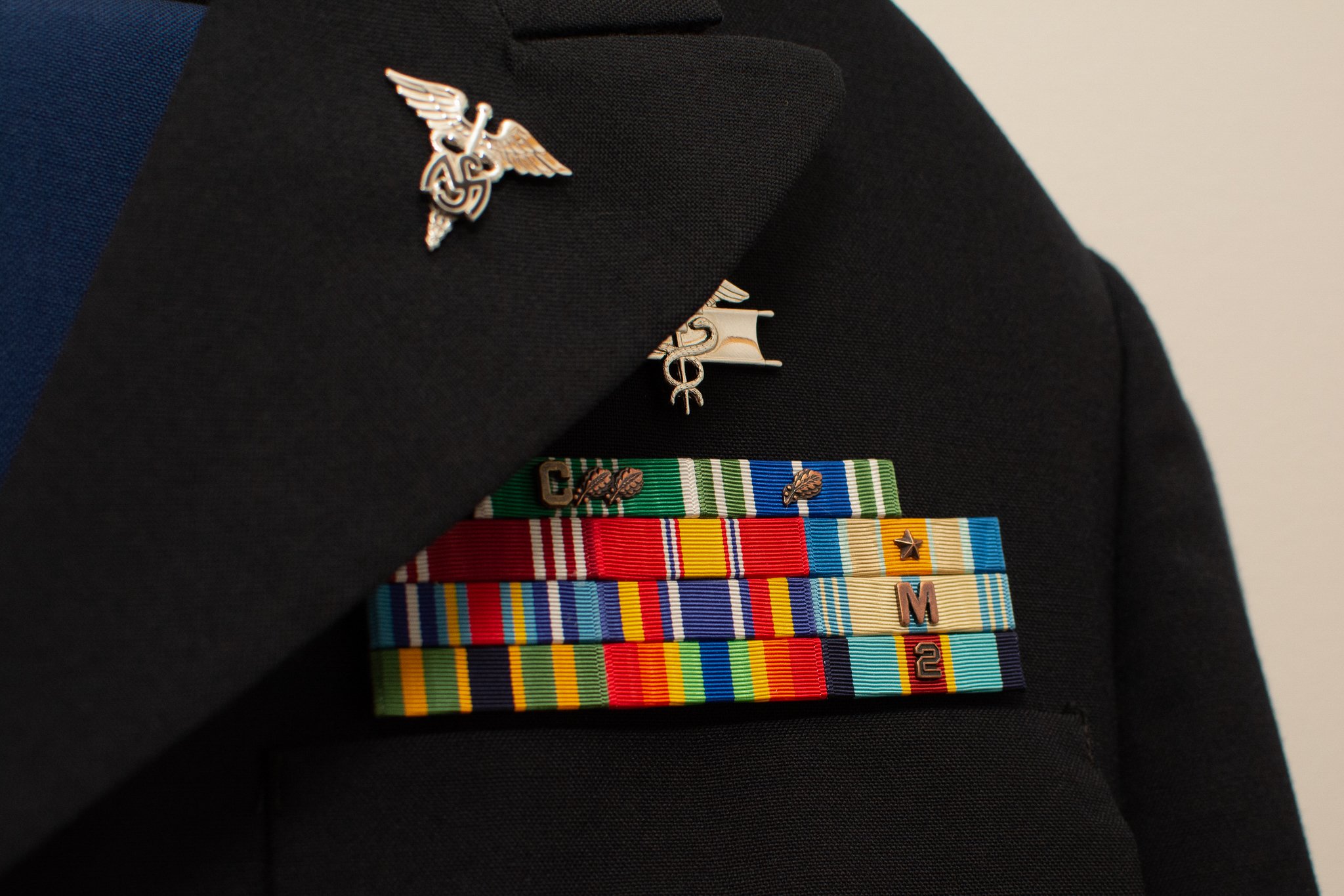 A military uniform jacket with various service ribbons and badges, including a silver badge with wings and a caduceus symbol.