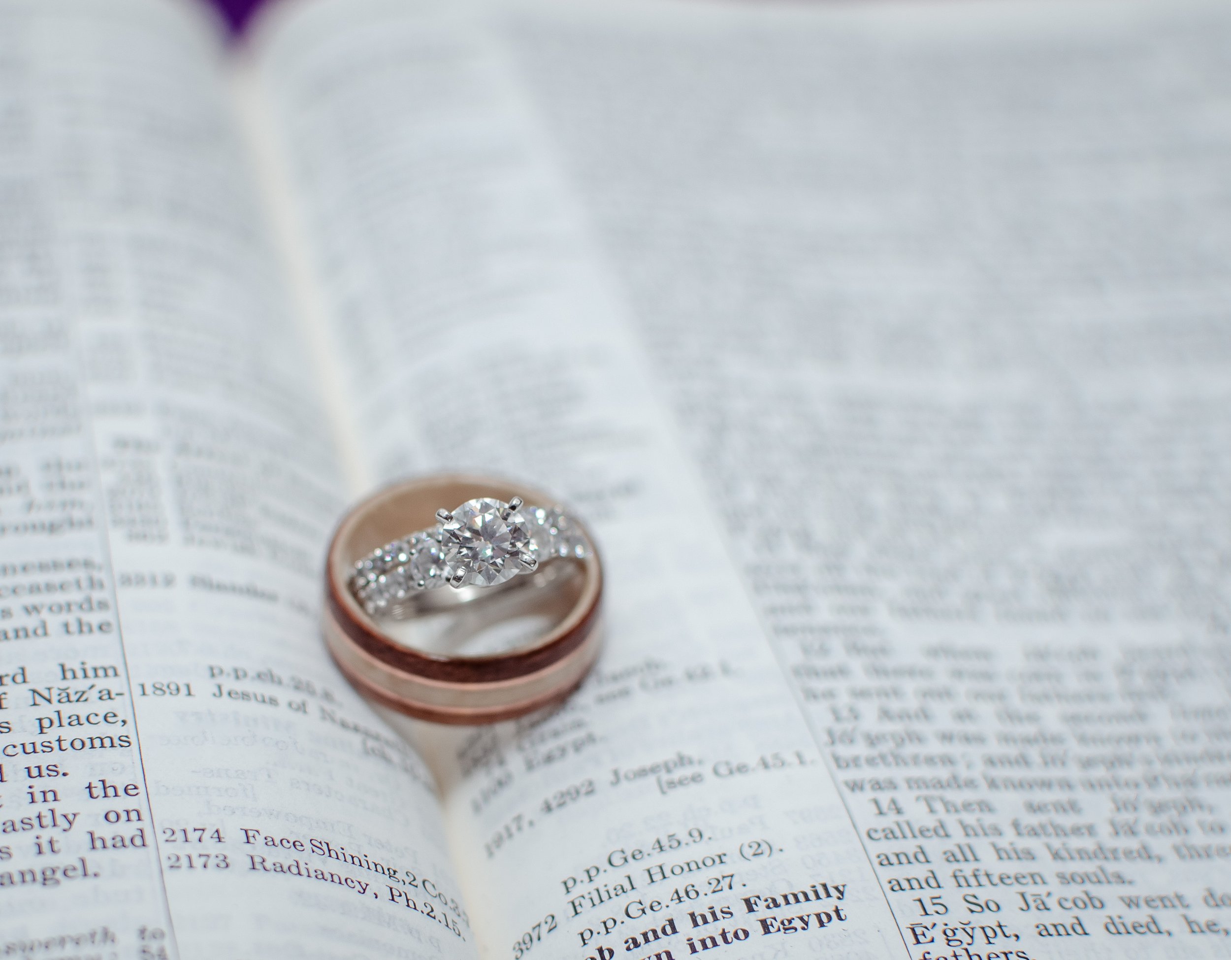 A diamond engagement ring and wedding band resting on an open book or dictionary.