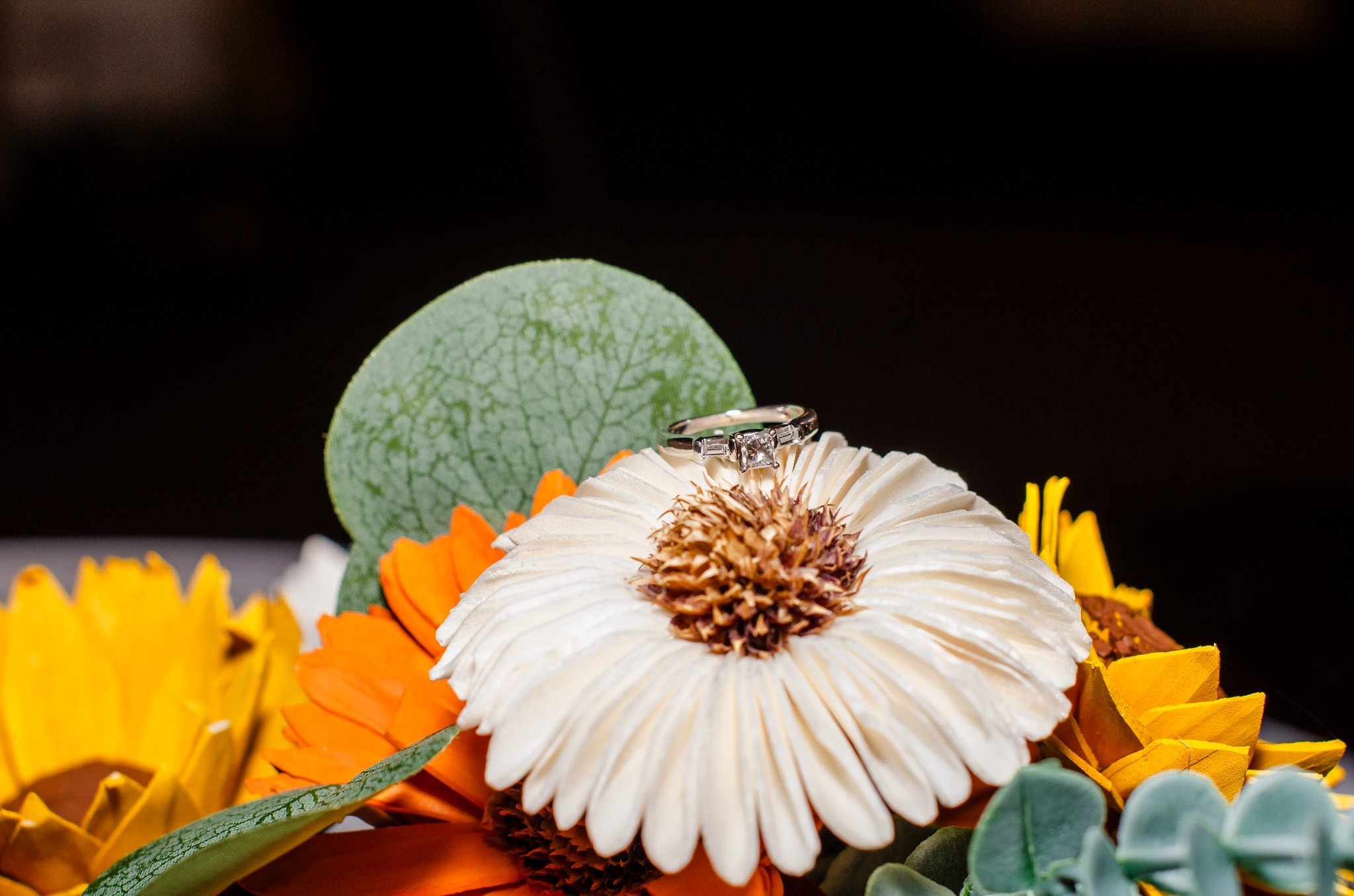 A white flower with a ring on it surrounded by orange, yellow, and green leaves and flowers.