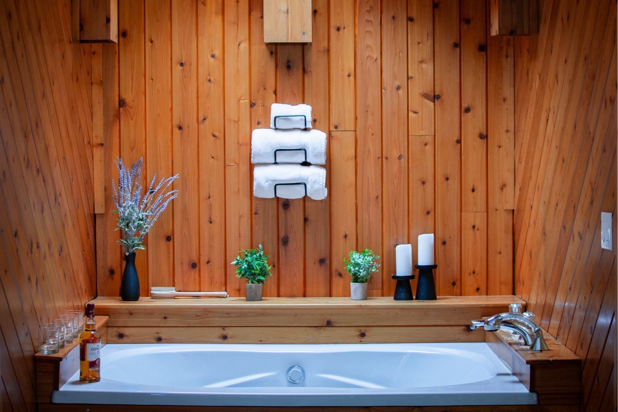 Wood-paneled bathroom wall with towels, candles, potted plants, bath products, and a bathtub.