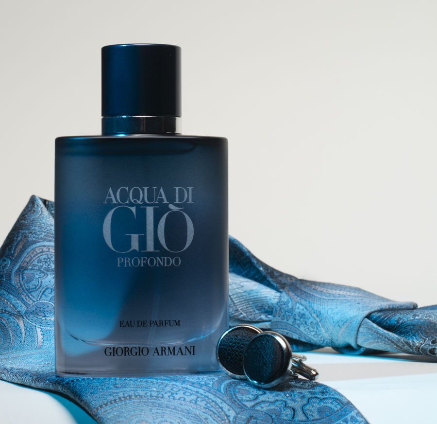 A blue bottle of Giorgio Armani Acqua di Giò Profondo perfume with matching cufflinks on a patterned blue cloth.