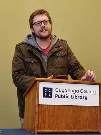 Jeremy Jusek stands at a podium while speaking and taking questions at a public event.