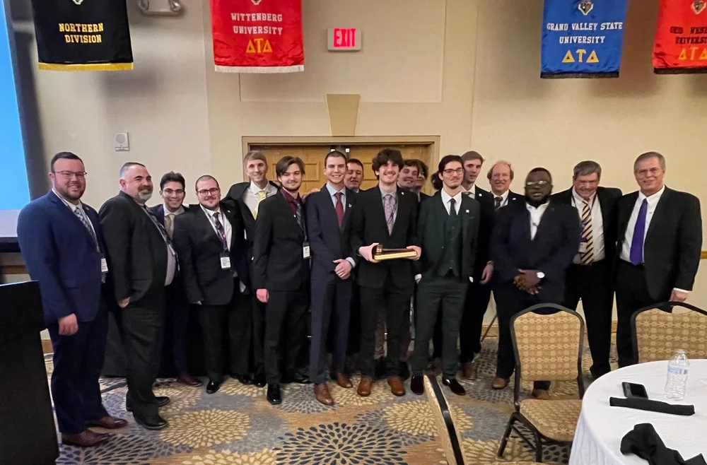 Alumni and undergraduates of Epsilon Upsilon Chapter stand in a line for a picture from 2023 at Northern Division Conference. Aaron Rohr is in the middle, holding the Court of Honor gavel.