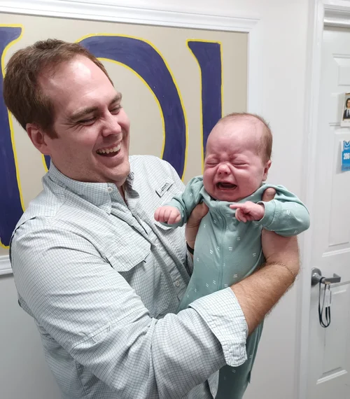 Alex smiles while holding his crying infant son in the back hall way of the Delt House in Marietta, Ohio.