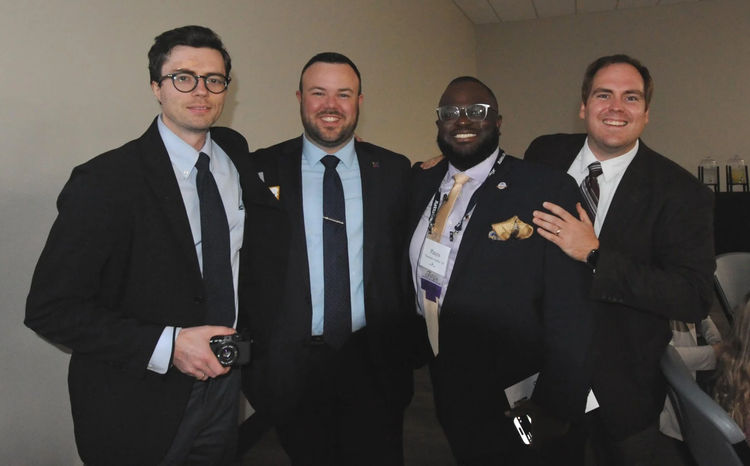 Four Delt alumni dressed in suits pose for a picture at a banquet dinner.
