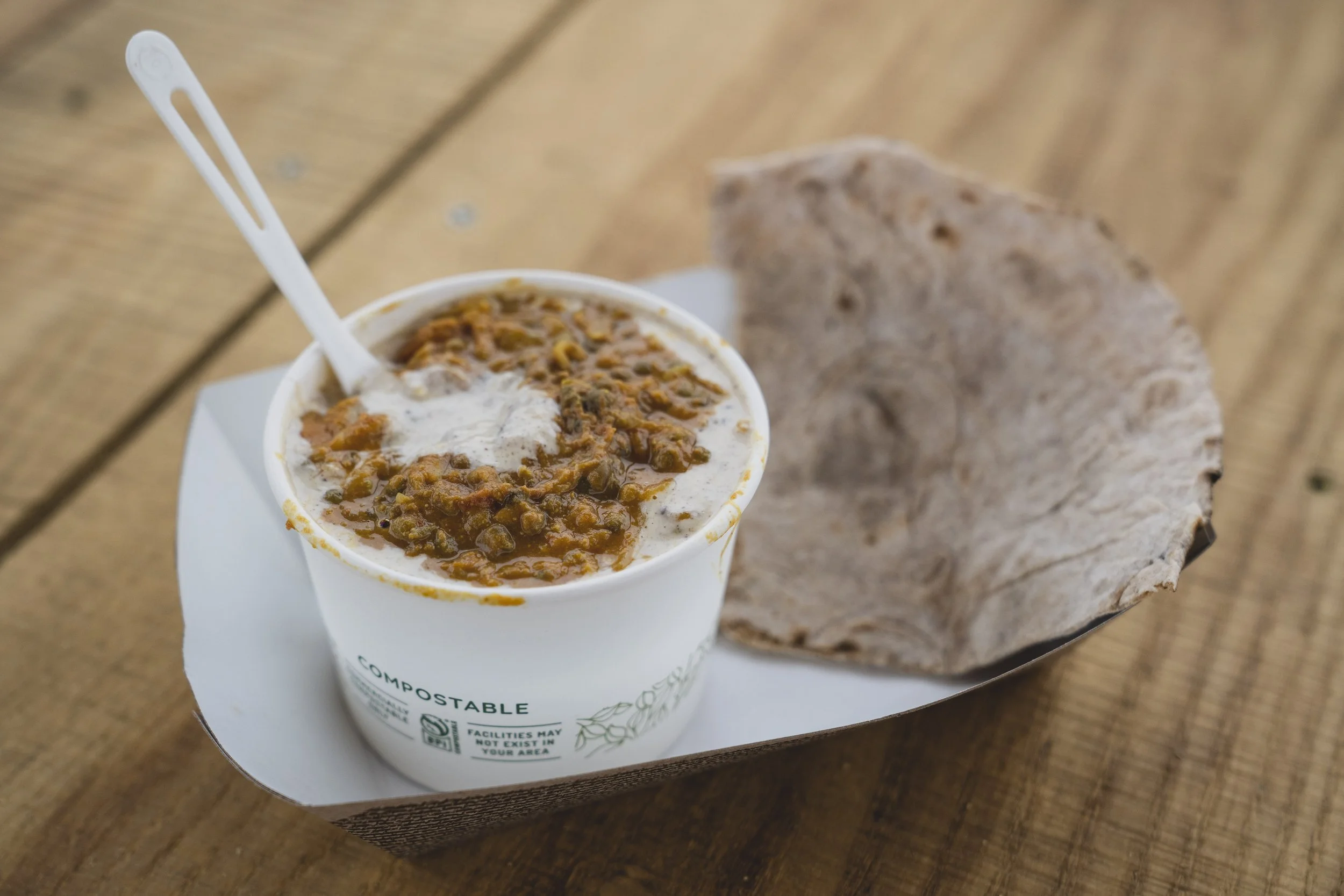 A cup of lentil soup with a side of flatbread on a tray, placed on a wooden surface.