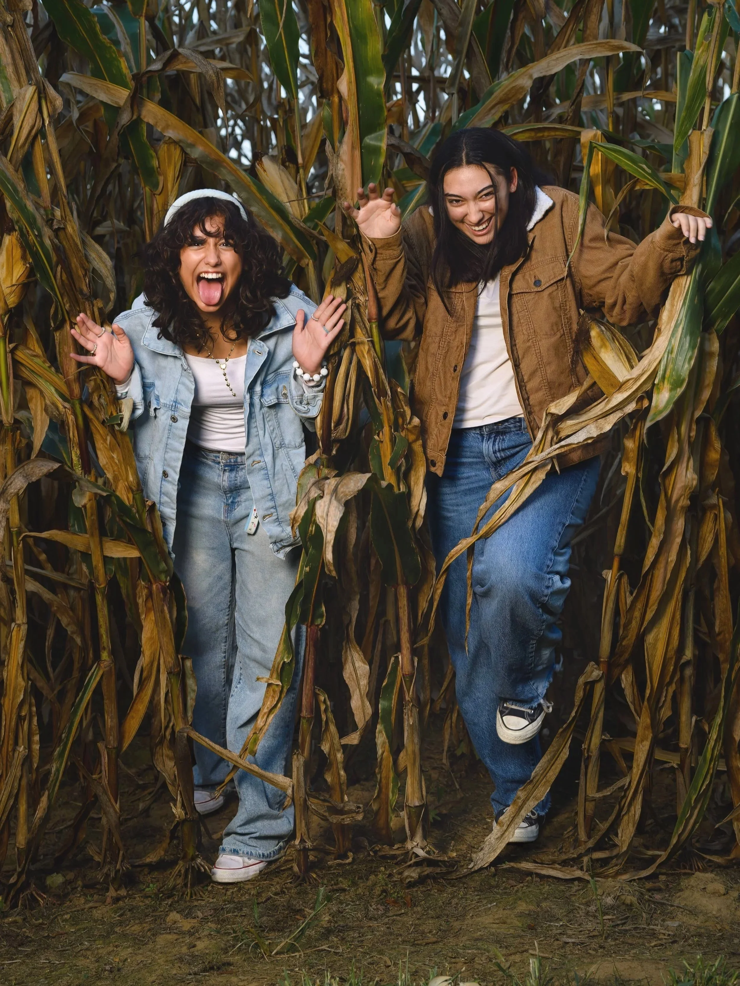 Two girls enjoying themselves in a cornfield, smiling and making playful gestures.