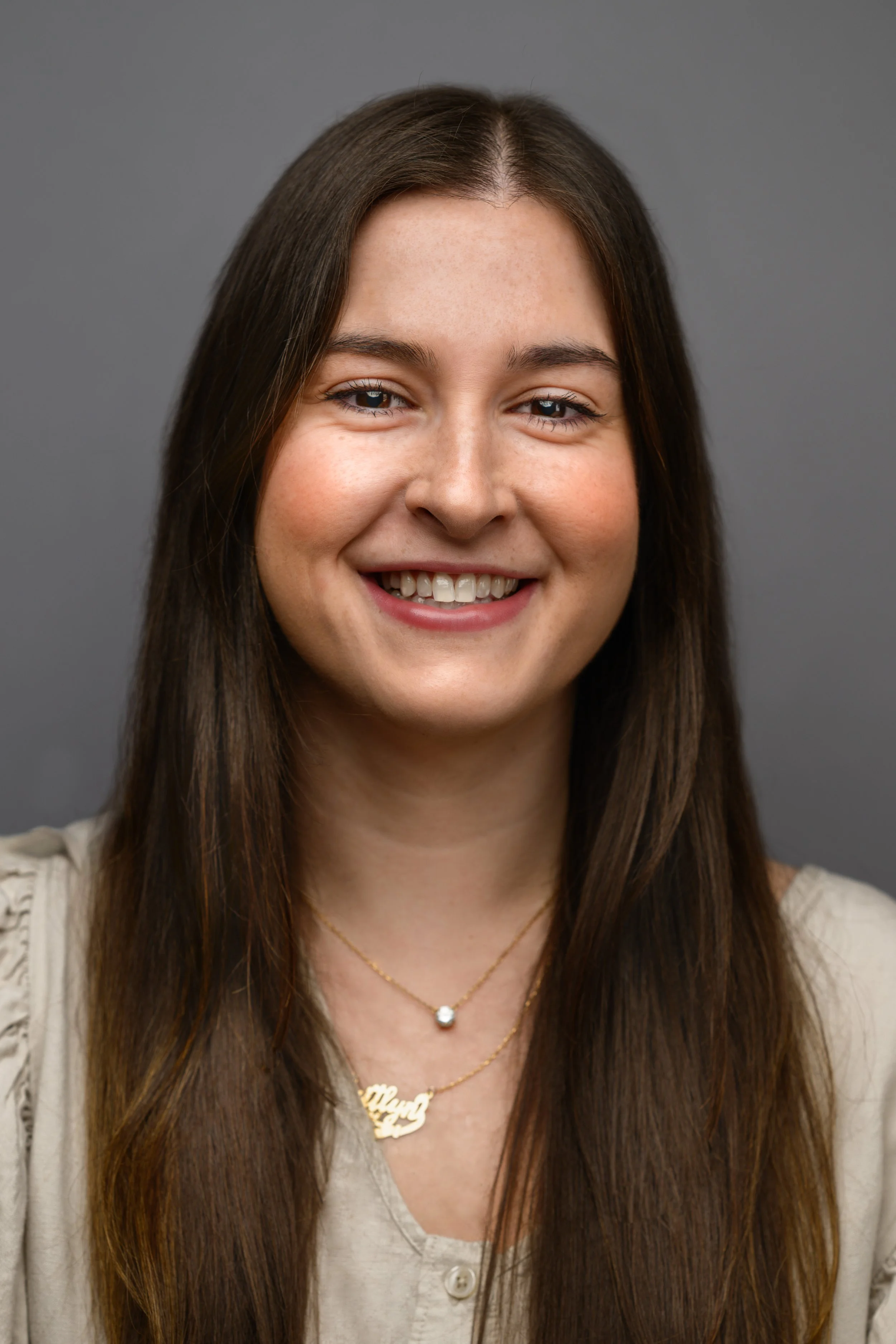 A smiling young woman with long brown hair against a gray background.