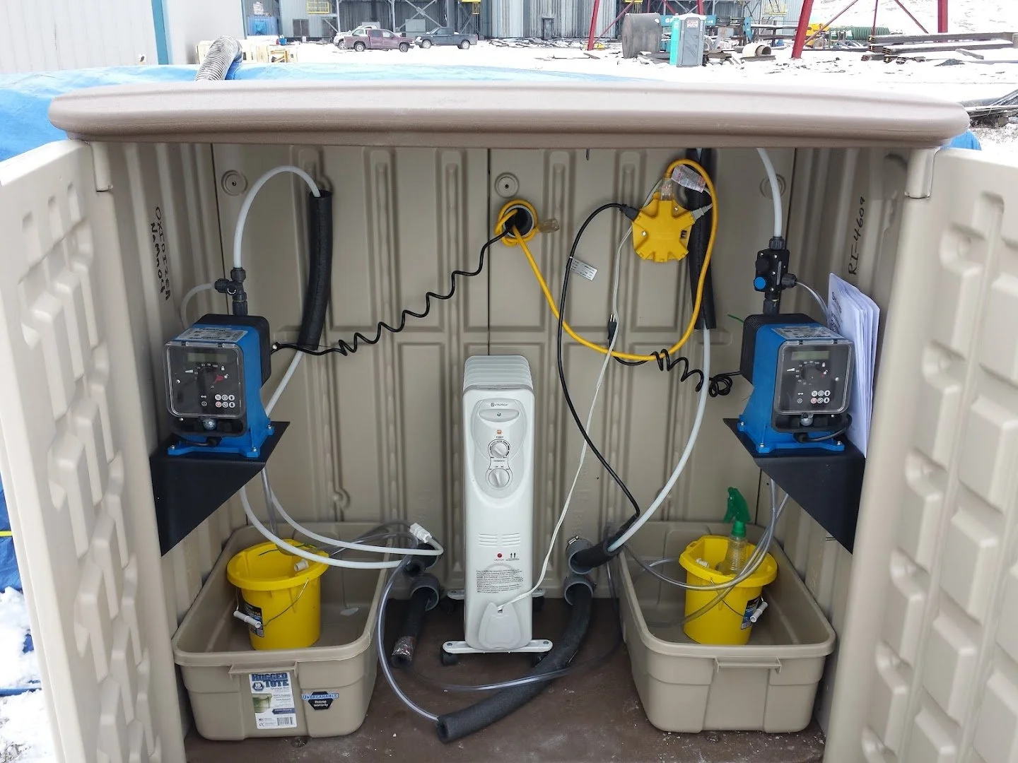 A self-contained water treatment or filtration system with pumps, hoses, containers, and electrical components inside an outdoor shelter.