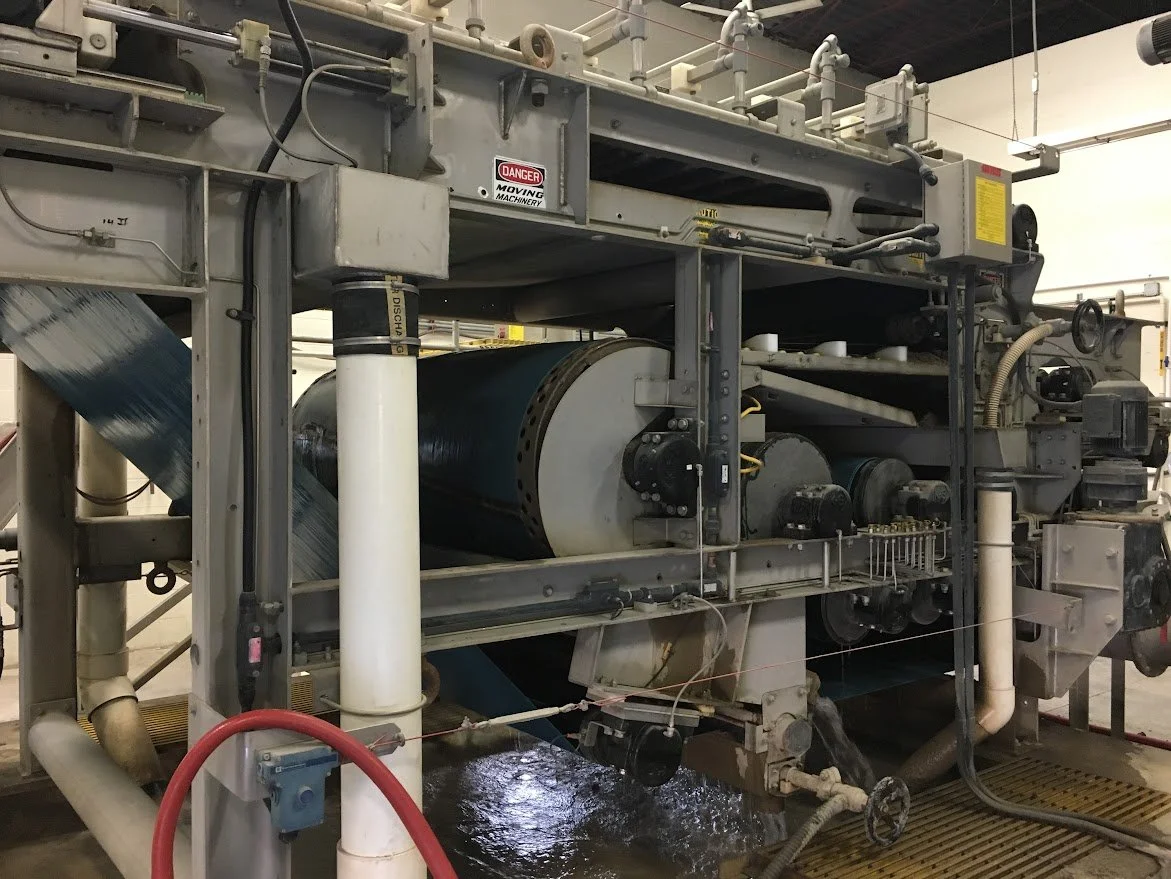 Industrial machinery with pipes, rollers, and warning labels in a factory setting.