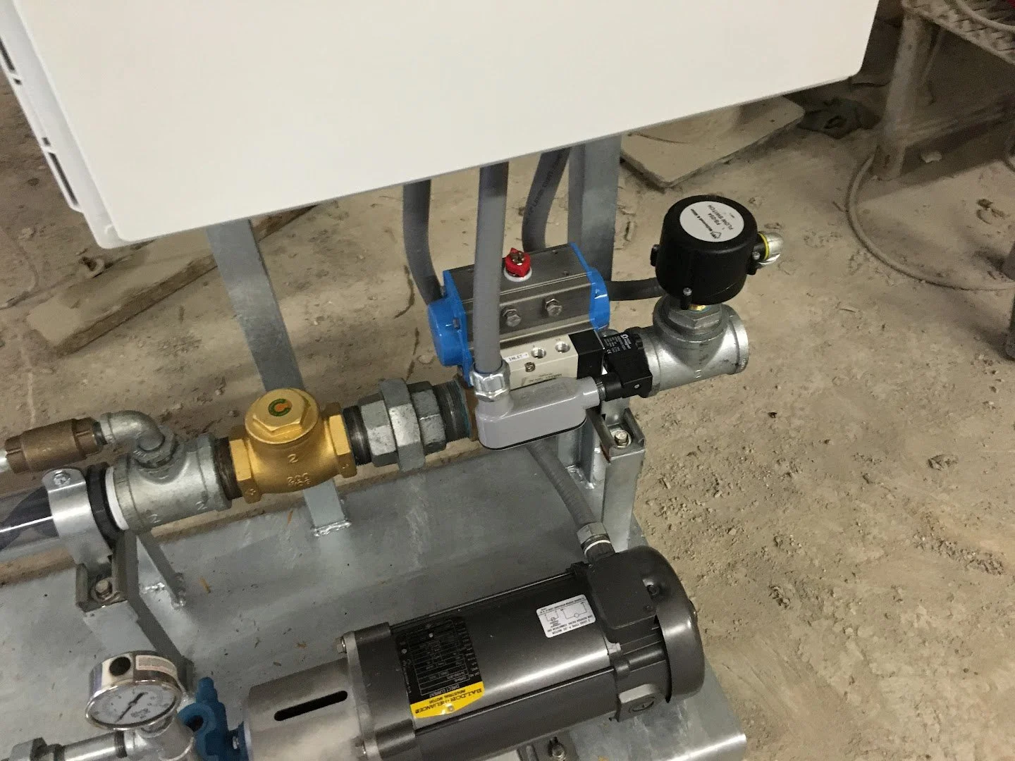 Close-up of industrial plumbing with pipes, valves, and a small electric motor on a concrete floor.