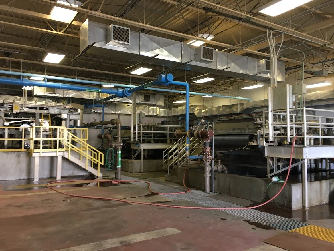 Industrial wastewater treatment tanks with pipes, hoses, and safety railings inside a processing plant.