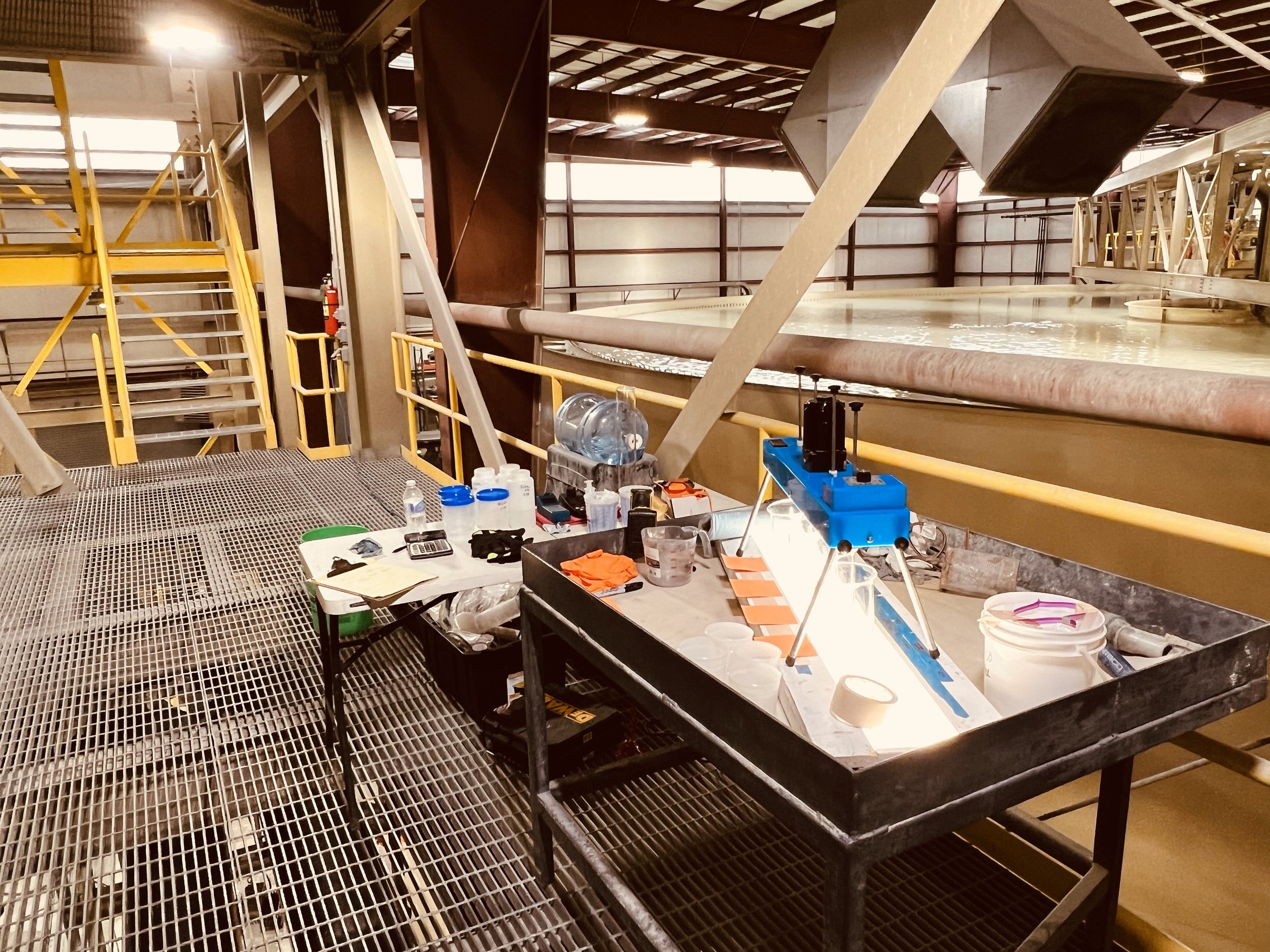 Laboratory setup with equipment, tools, and supplies next to a large industrial water channel inside a factory building.
