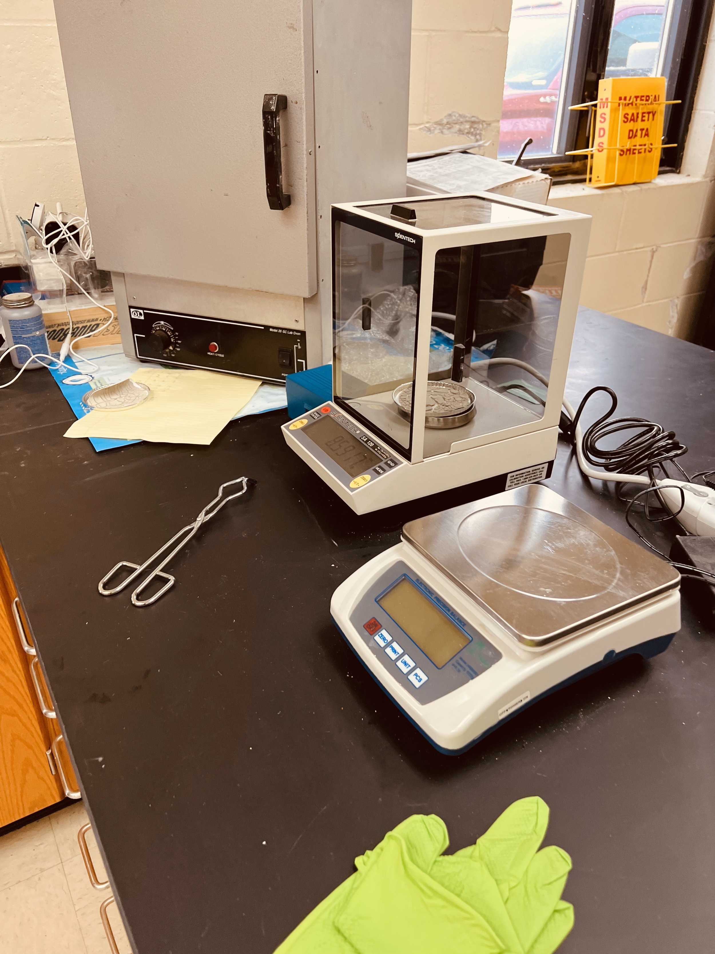 Laboratory workspace with a digital balance, an enclosed gravity tester, and other lab equipment on a black countertop.