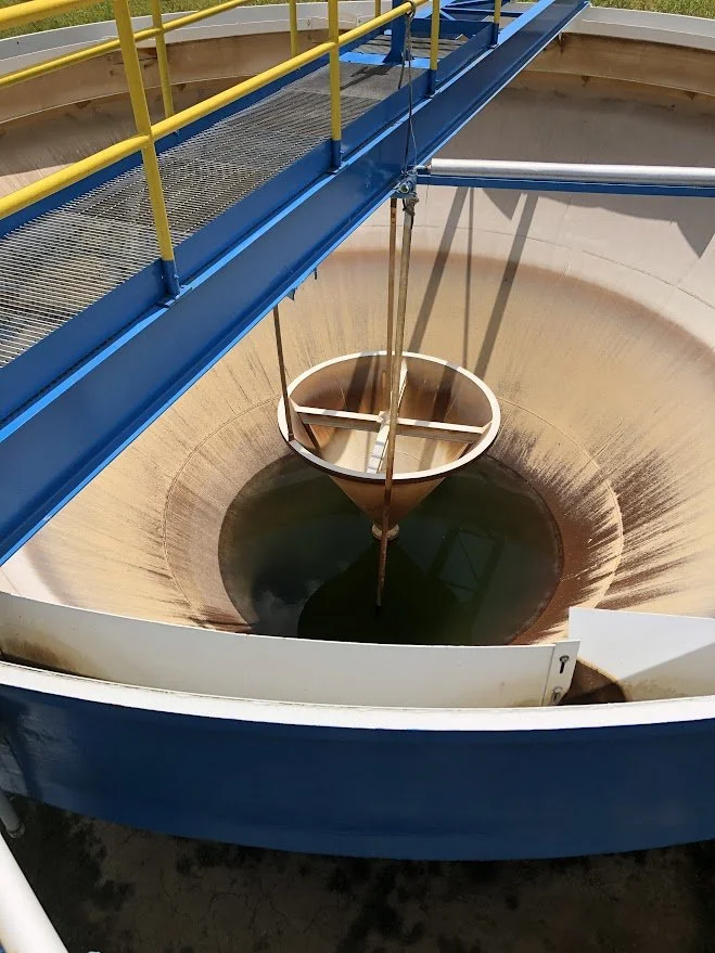 Industrial tank or bioreactor with a stirring mechanism and brown liquid, surrounded by a blue and yellow safety railing.