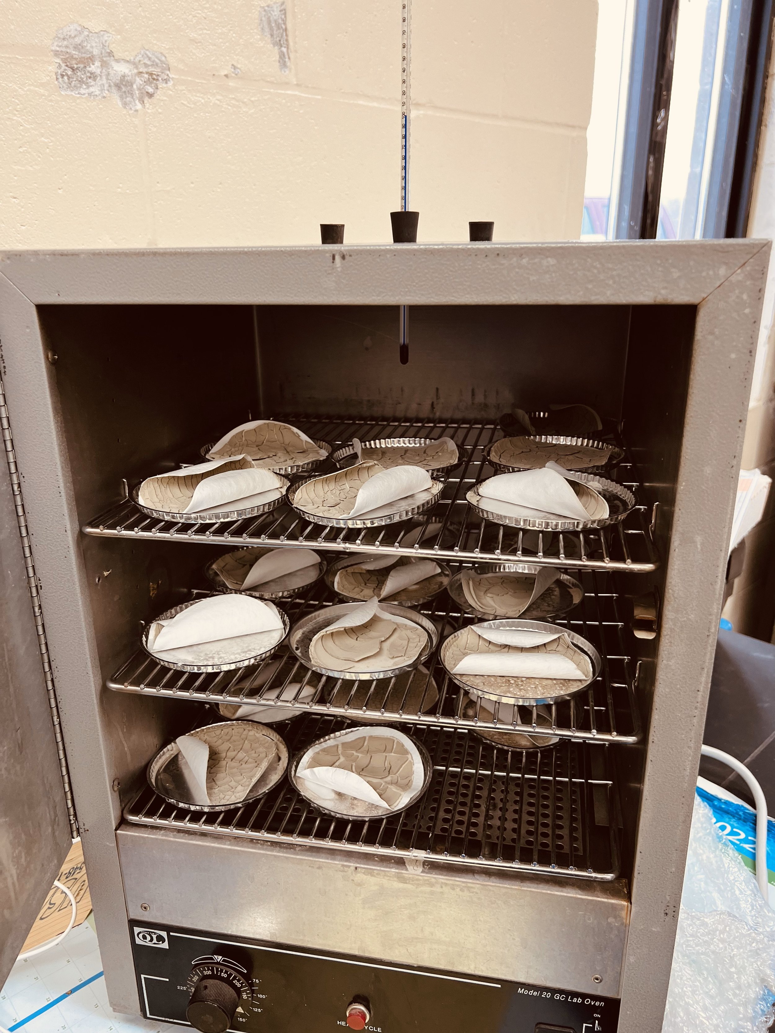 A small laboratory oven with multiple ceramic dishes on metal racks inside.