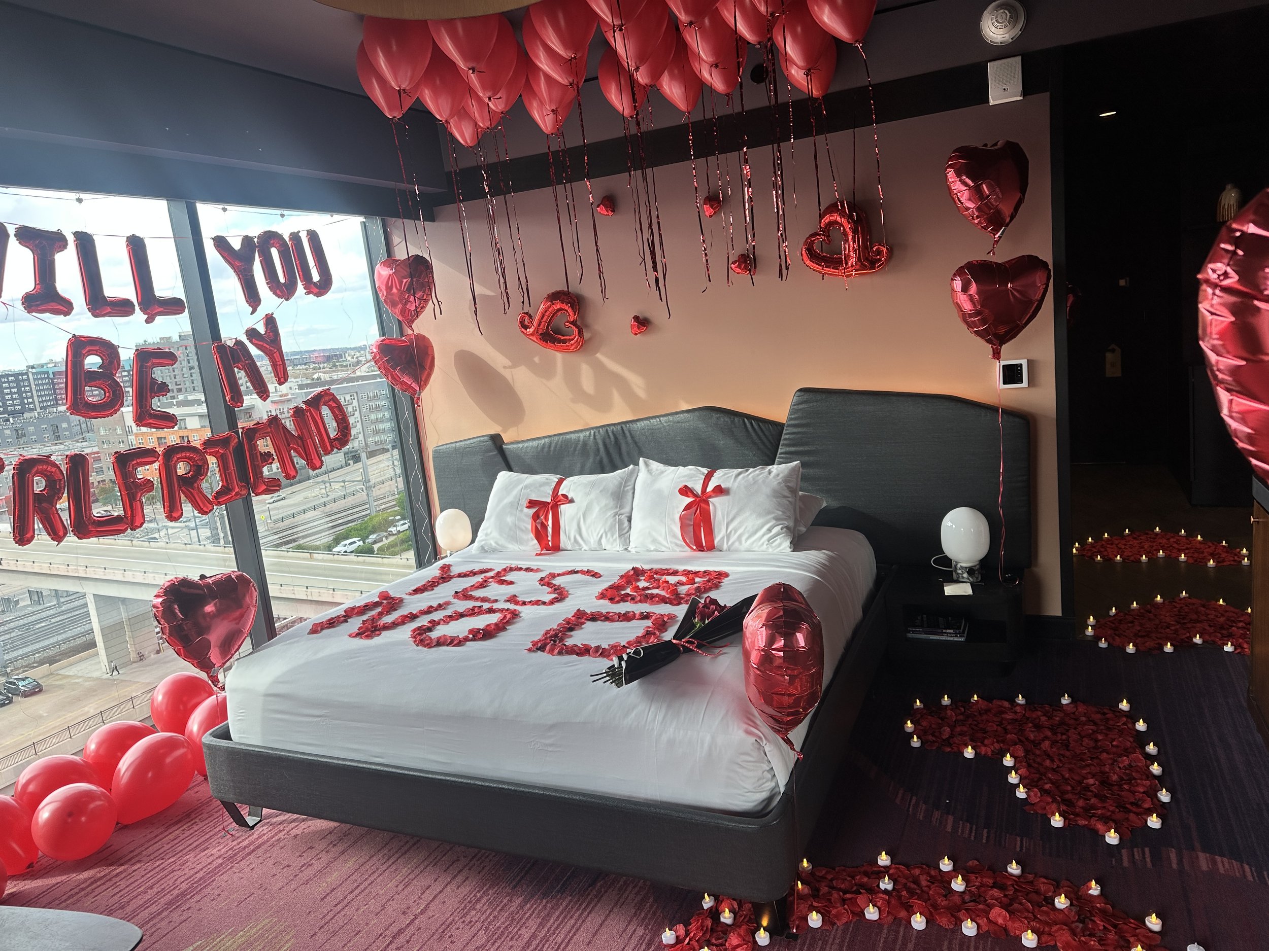 Decorated hotel room with pink and white balloons, silver '26' balloon, 'Happy Birthday Mamas' balloons, pink bouquet, and balloons on bed for a birthday celebration in Denver, Co.