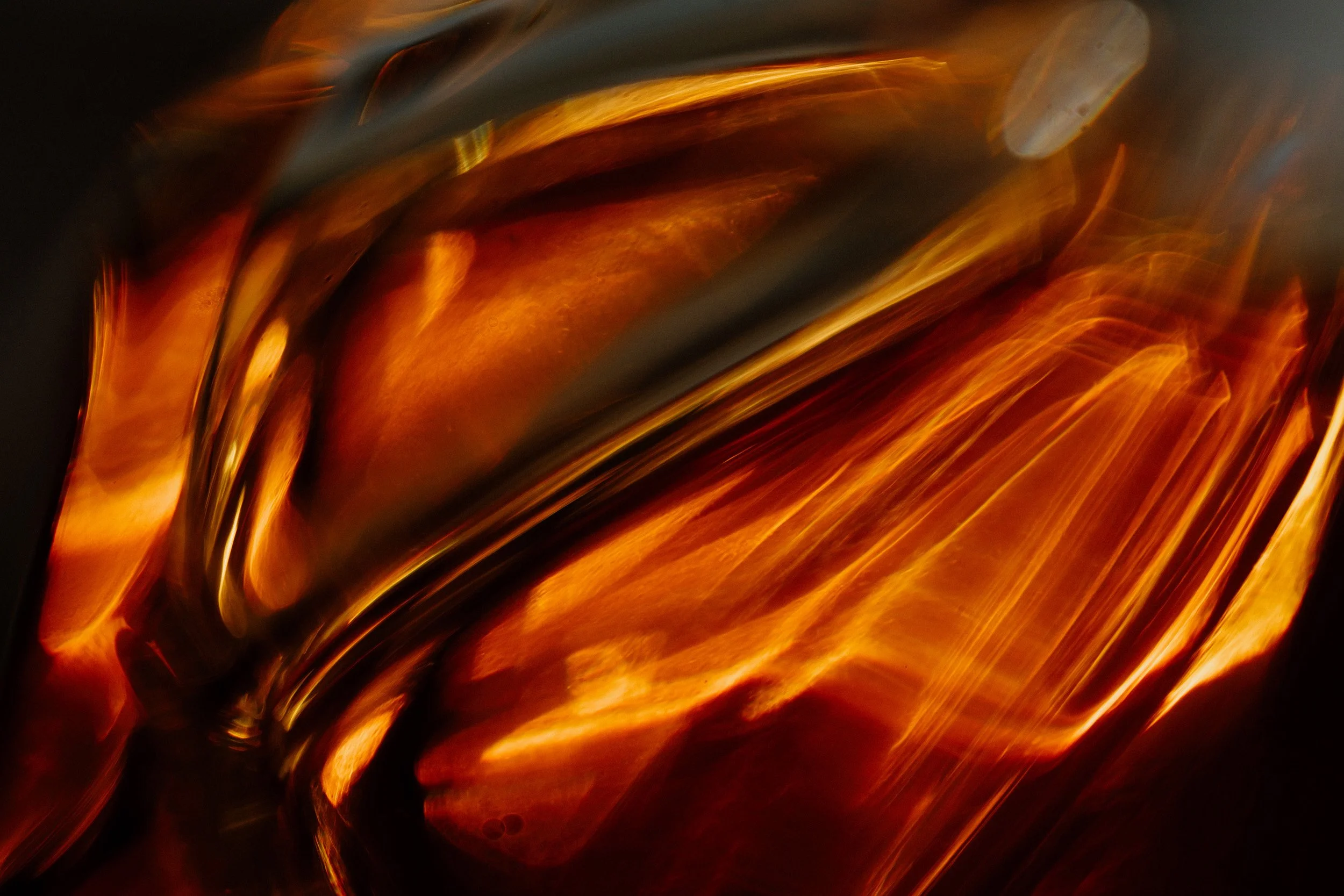 Close-up photograph of flowing molten glass with fiery orange and yellow hues and dark shadows.