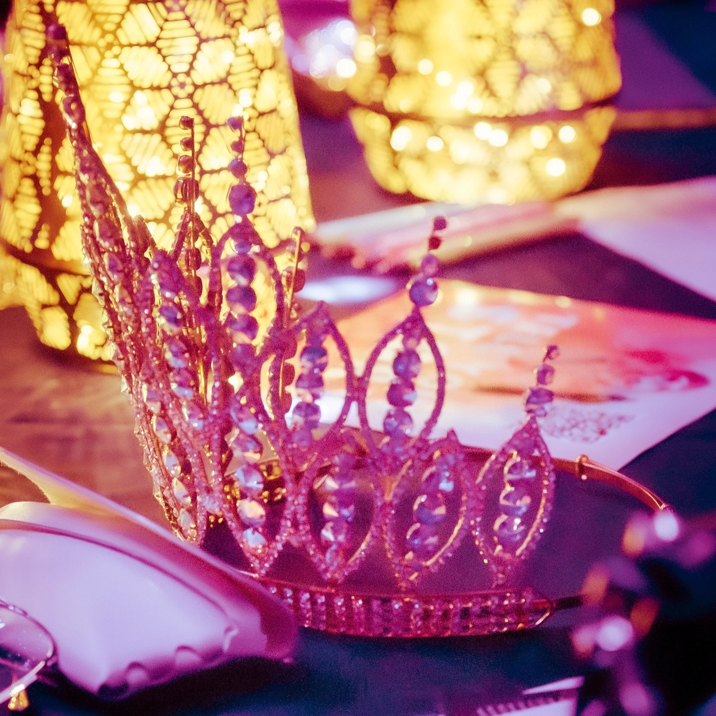 Close-up of a decorative lamp with yellow patterned light and purple beaded jewelry or decoration in front, on a pinkish surface with a purple background.
