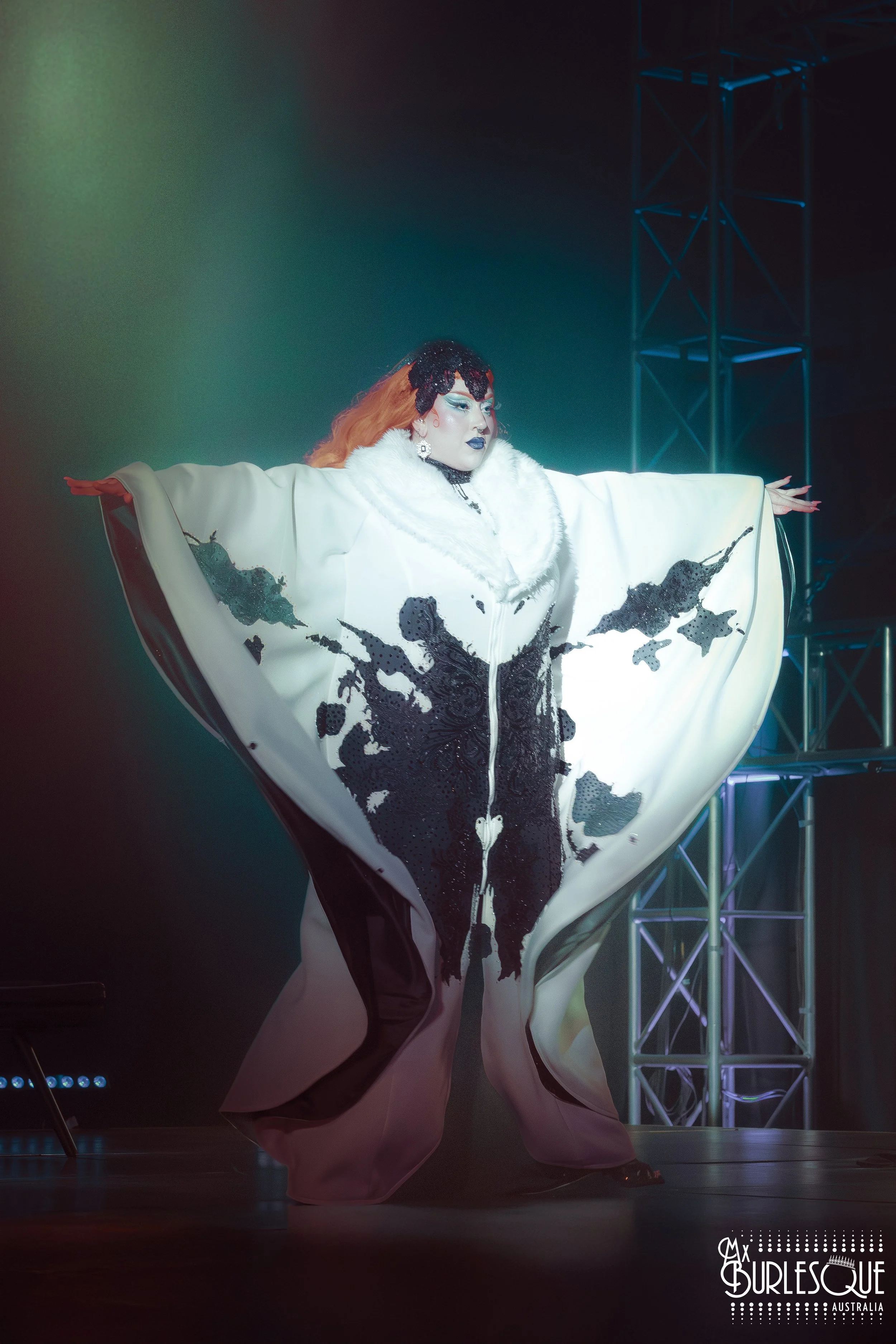 Performer wearing elaborate white and black costume with outstretched arms on stage at Burlesque Australia event.