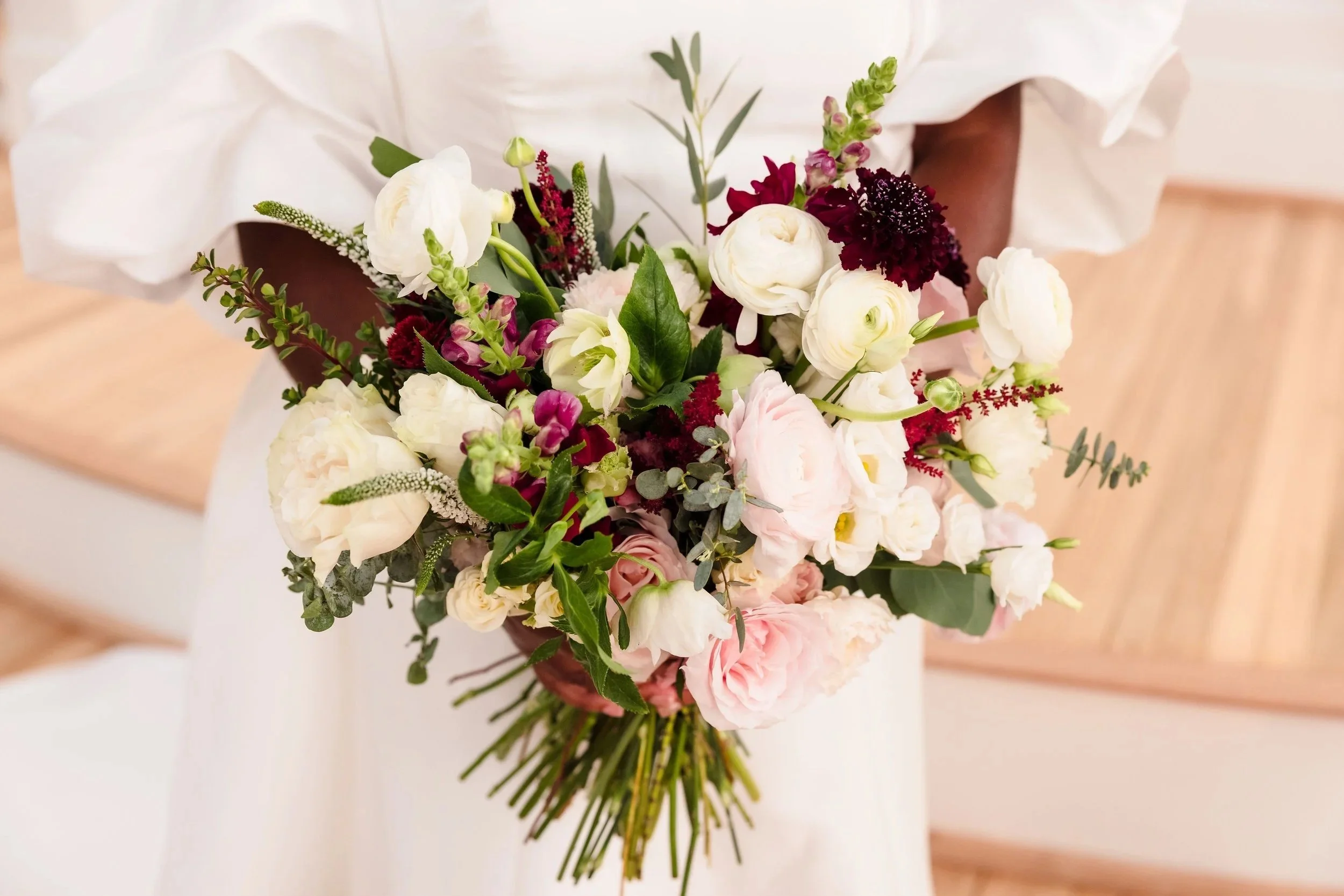 Bridal bouquet with white, pink, and dark purple flowers and green foliage.