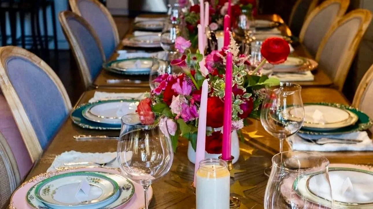 A dining table set for a formal gathering with floral centerpieces and candles.