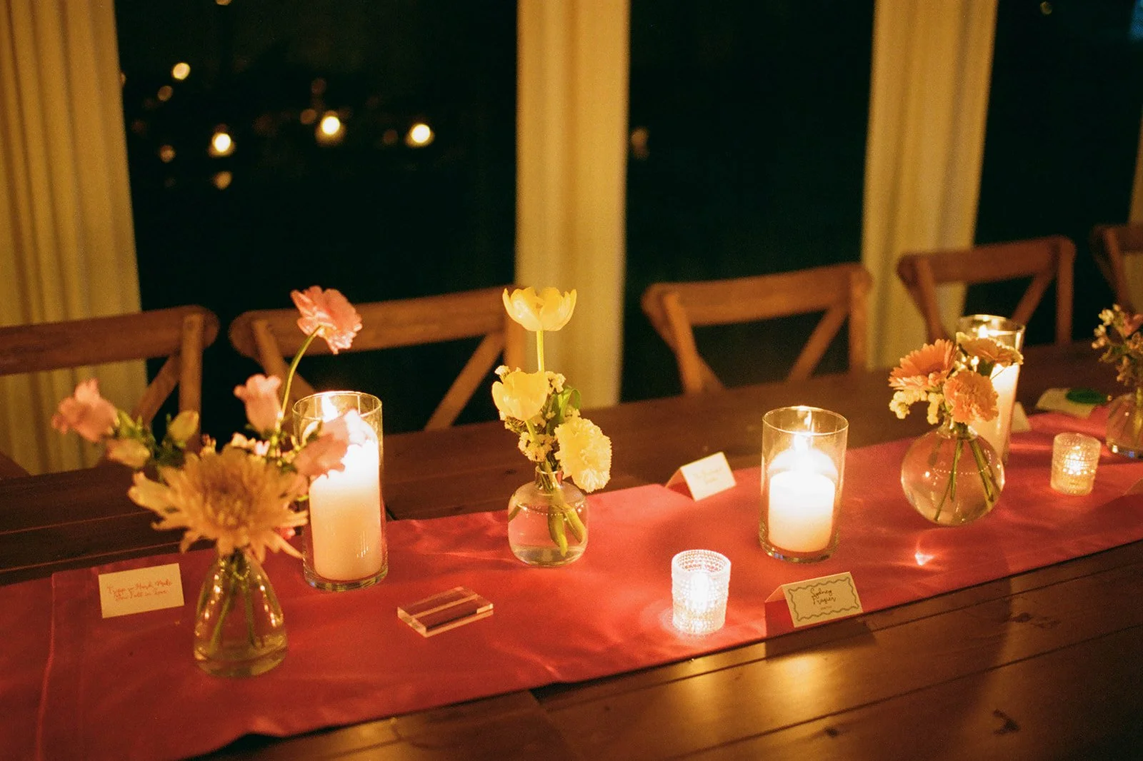 Elegant dinner table decorated with pink and white flowers in vases, lit candles, and pink table runner