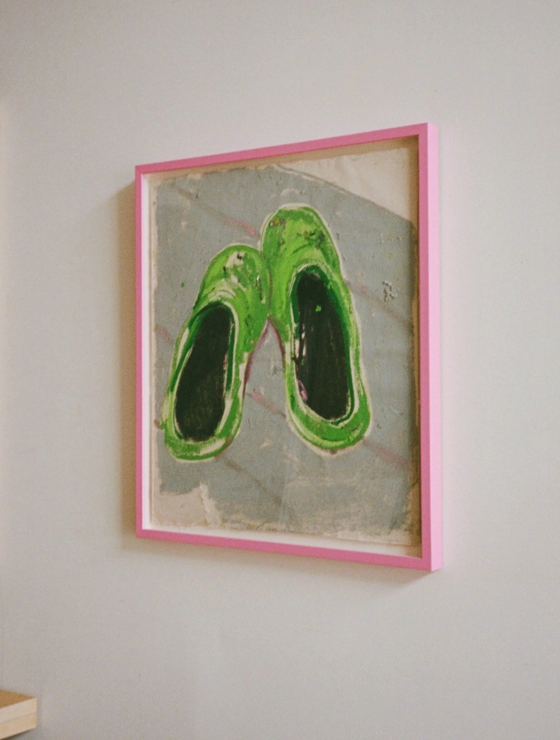 Painting of green slippers with black insoles framed in pink on a white wall