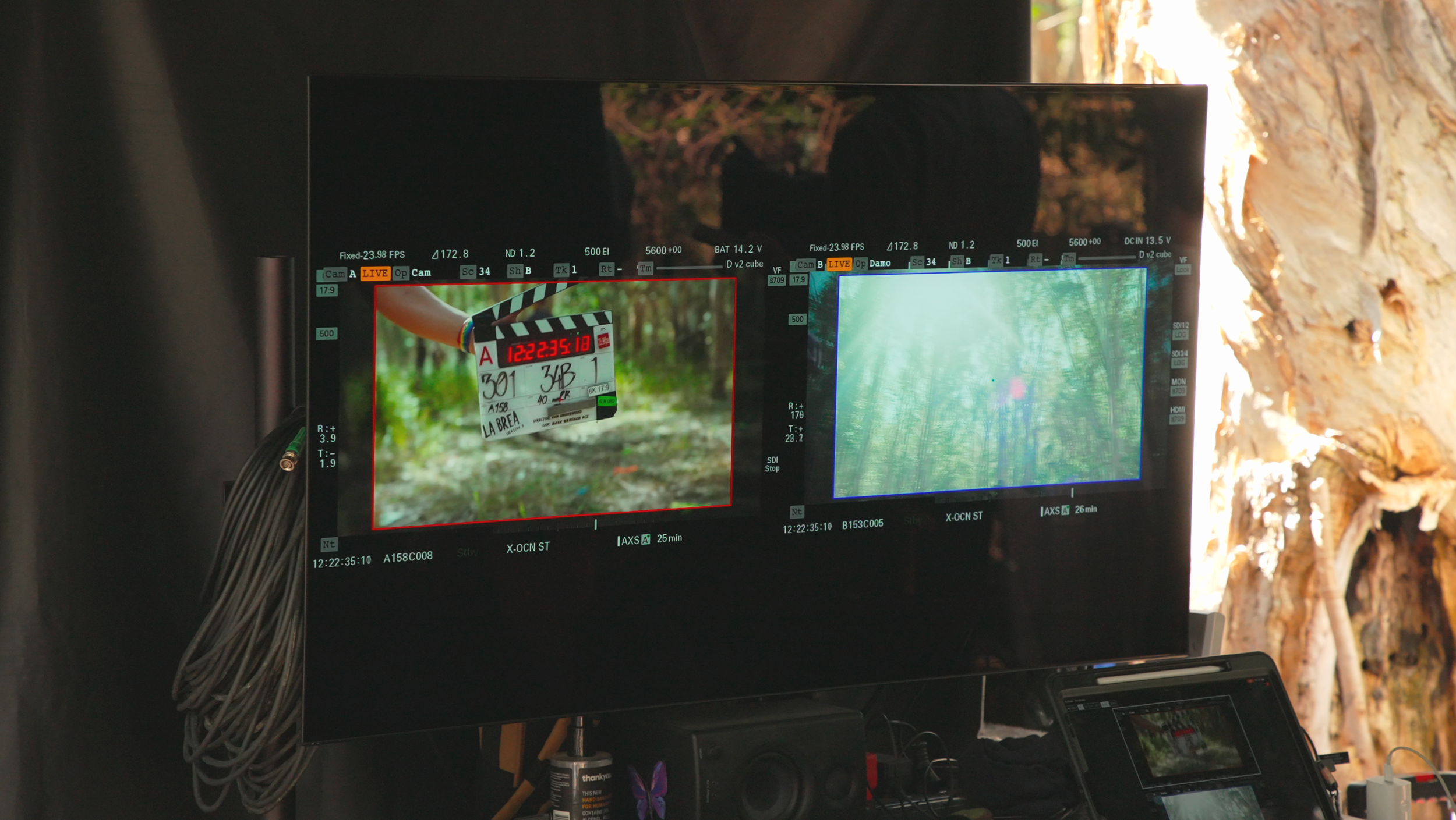 A camera monitor shows a scene from a film or video shoot, with a clapperboard in focus. The background includes trees and outdoor scenery.