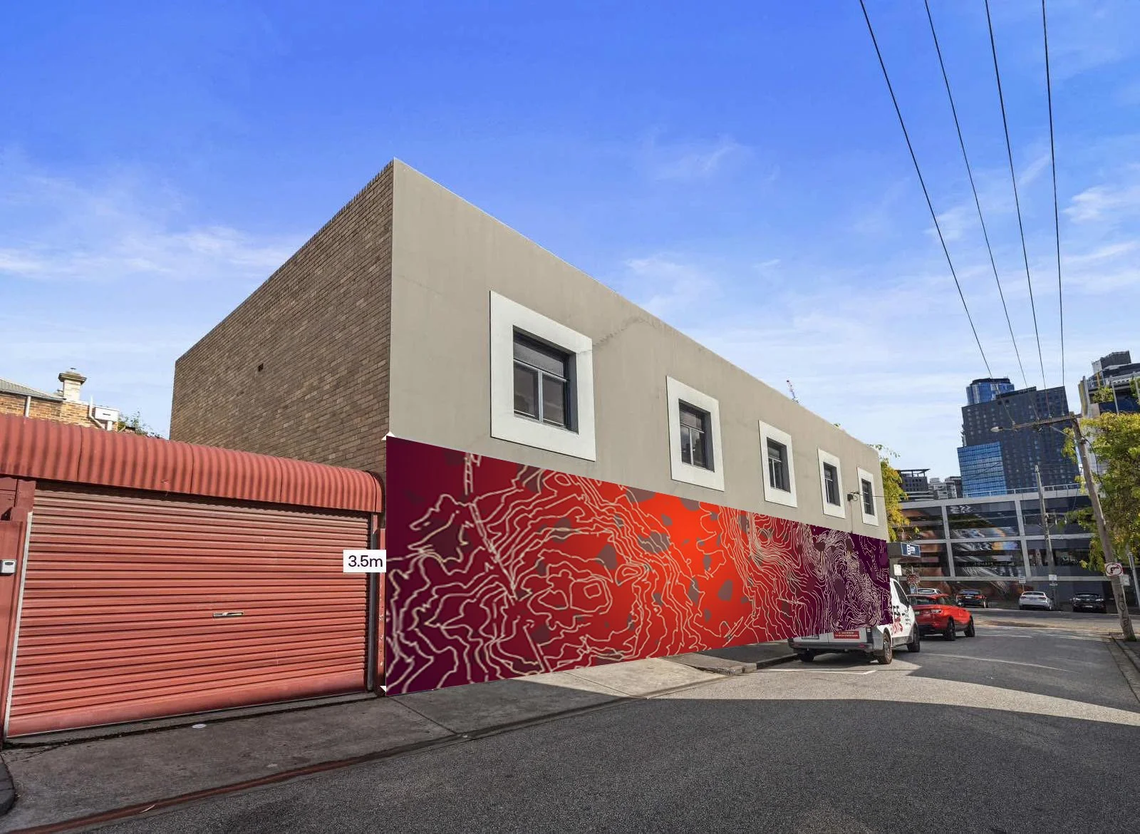 A building under construction with a beige second floor, a red garage door, and a colorful mural with topographical map design along the lower part of the structure in an urban area.