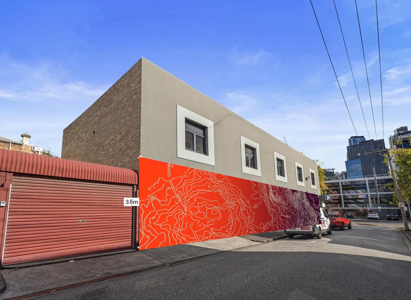 Modern building with a two-story beige and brick exterior, located on a city street with parked cars and a mural featuring topographical lines in orange and purple at its base.