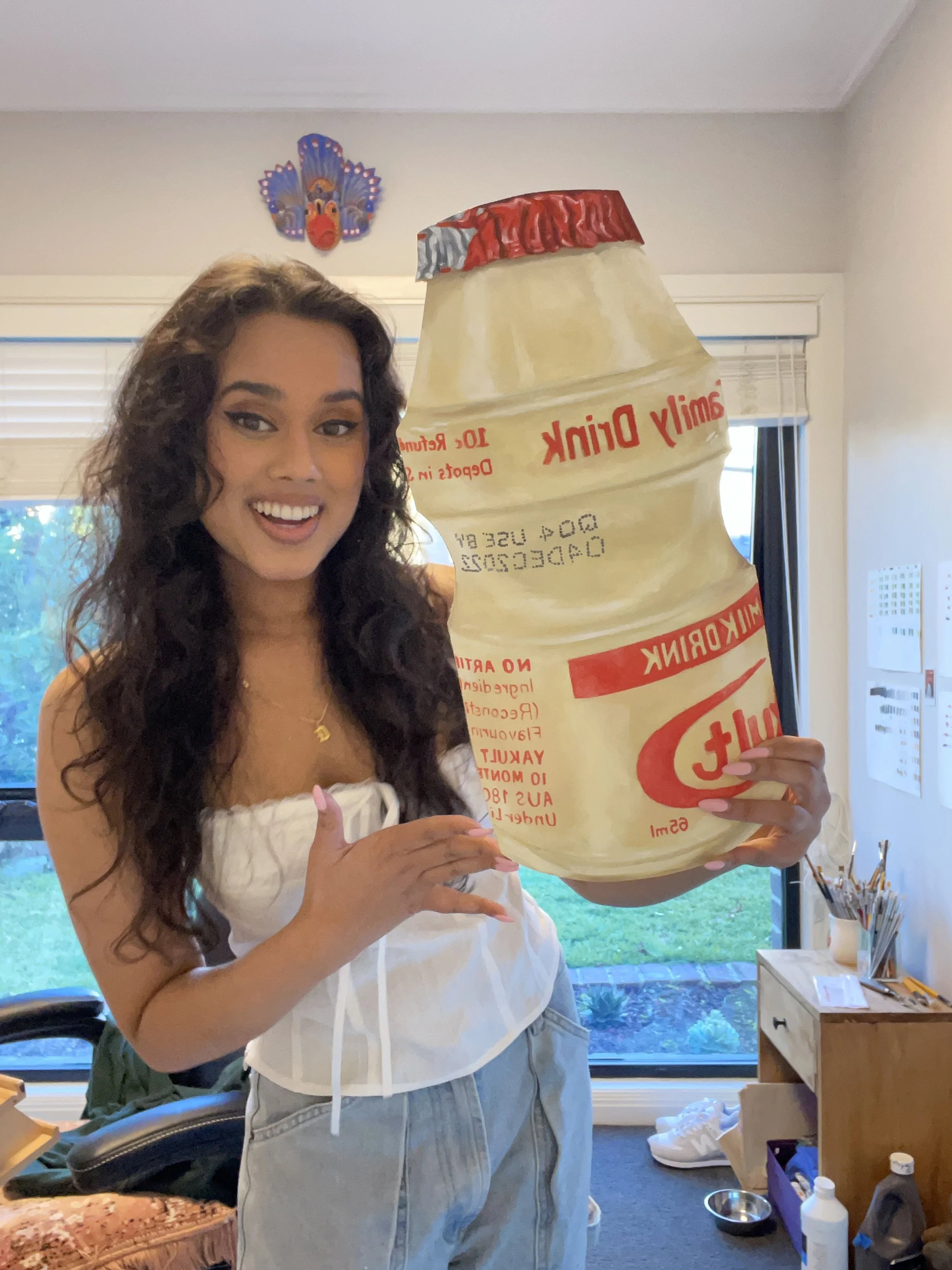 Dilara holding a large yakult bottle painting in the studio.