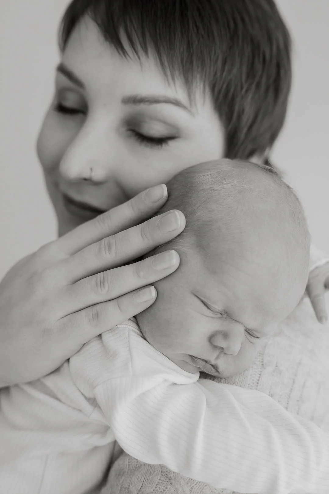 Nuori nainen halailee ja suukottaa pientä vauvaa, joka nukkuu hänen olkapäänsä päällä, mustavalkoinen kuva.