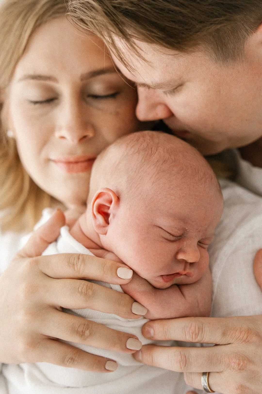 Äiti ja isä halaavat ja suukottavat vastasyntynyttä, jonka pää lepää äidin käsivarren päällä.