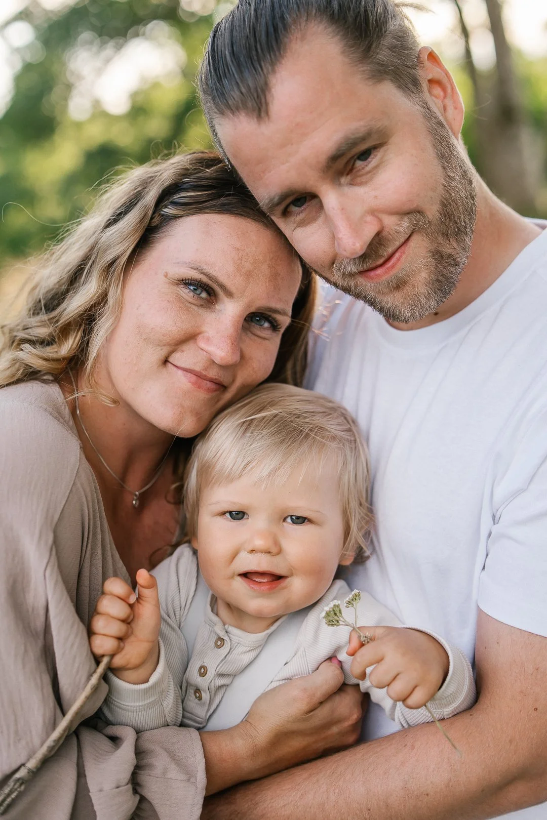Näyttävä kuvasarja raskaana olevasta naisesta, miehestä ja lapsesta, jotka hymyilevät ulkona luonnossa ja ovat lähekkäin.