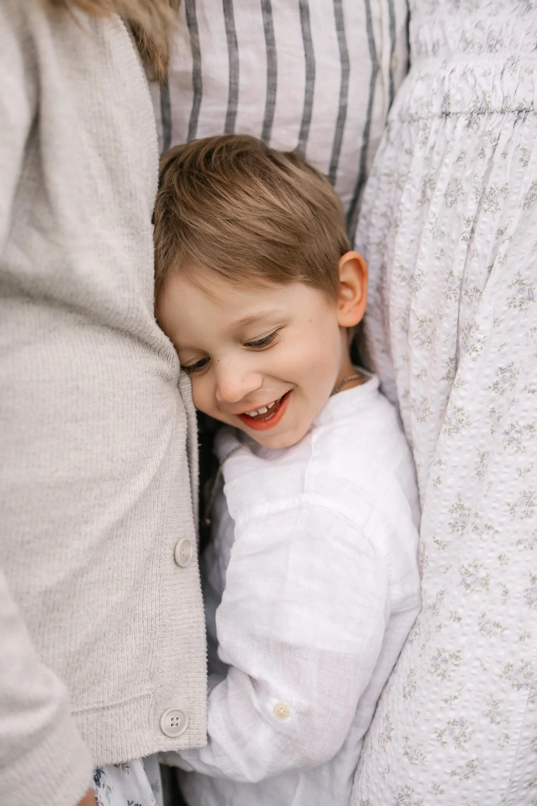 Hymyilevä poika, joka on sylitetty isän ja äidin lähellä.