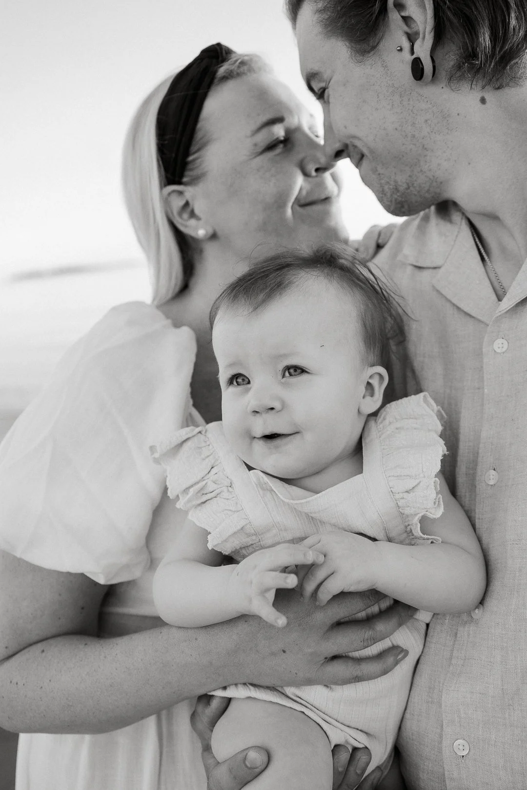 Perhe iloisen näköinen ja katsoo toisiinsa, pieni lapsi katsoo sivuun ja hymyilee