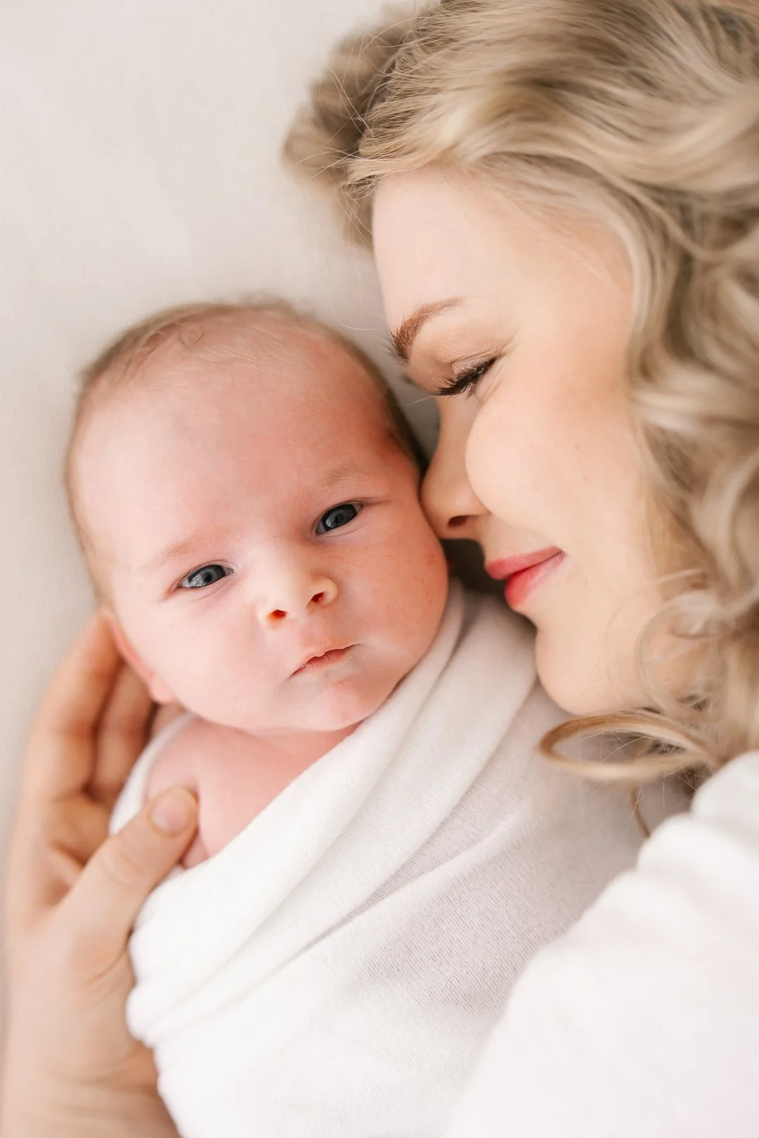 Äiti ja vauva lepäilevät lähekkäin, äiti suukottaa vauvaa poskelle.