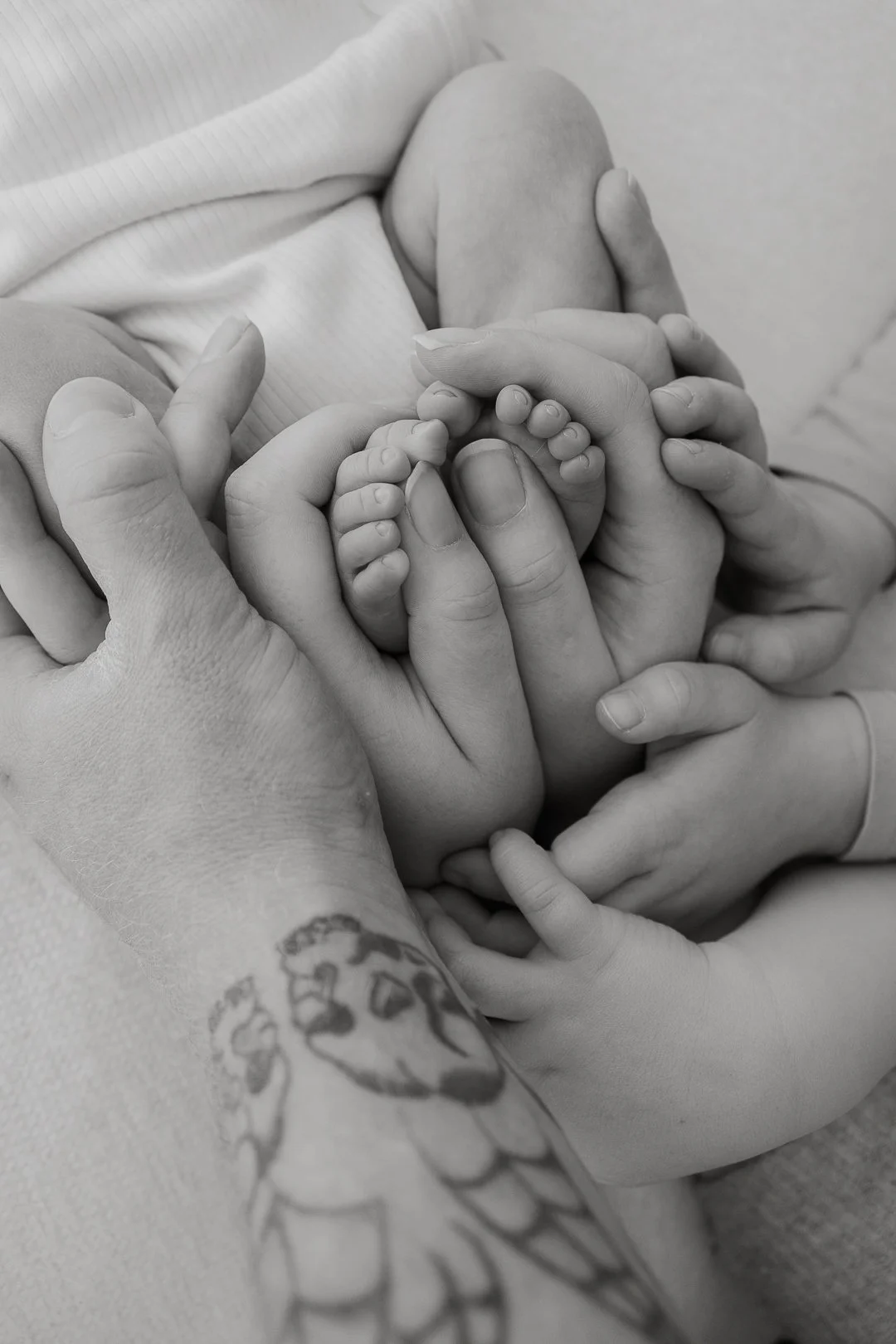 Mustavalkoinen kuva, jossa useat ihmiset, aikuinen ja lapsi, pitää käsiään ja pientä vauvaa, jonka sormet ovat näkyvissä.