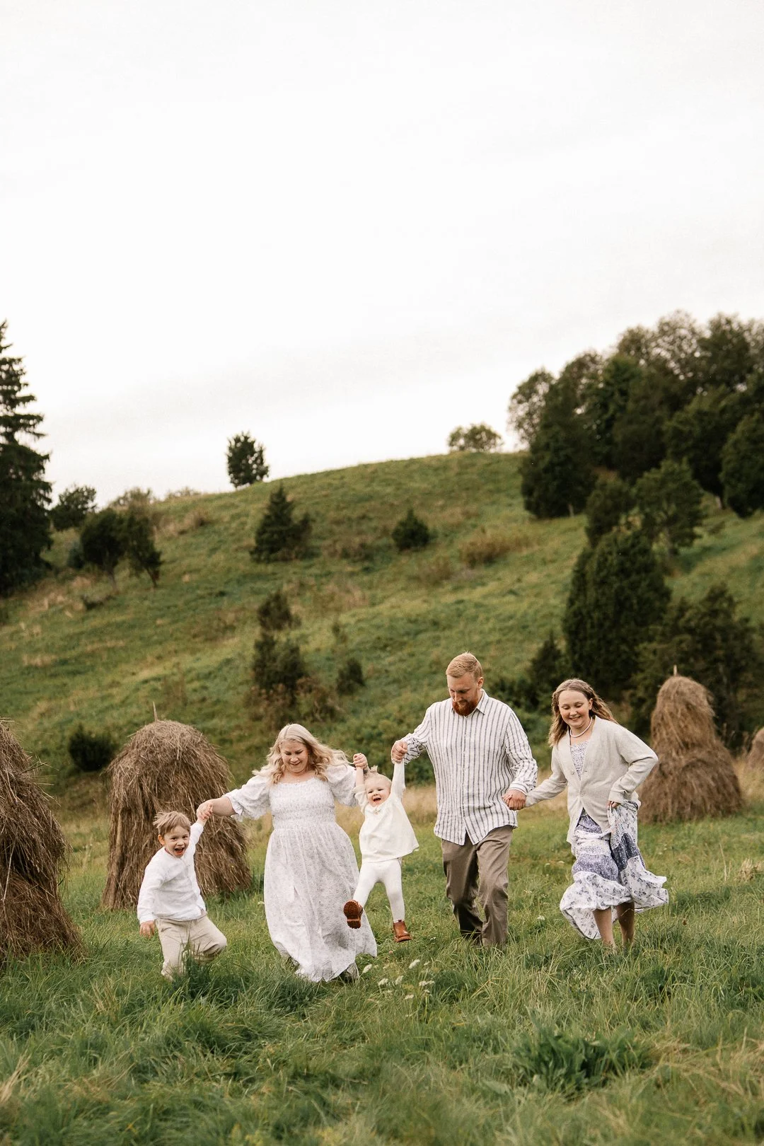 Perhe kävelee yhdessä pelloilla näkyen heinäkasoja ja puita taustalla.