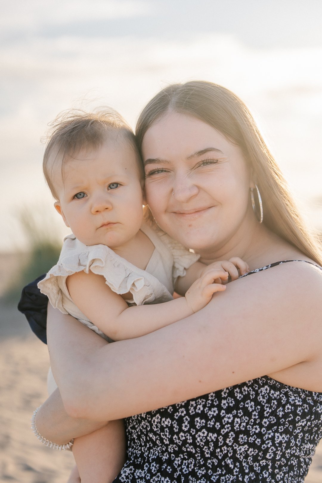 Nuori nainen ja pieni lapsi hymyilevät ja halaavat toisiaan valokuvassa ulkona auringonlaskun aikaan.