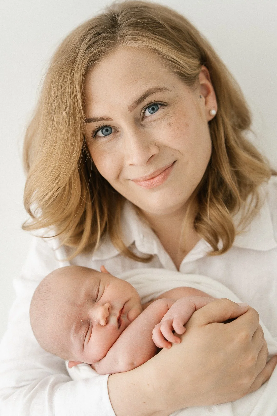 Nainen hymyilee ja pitää sylissään vastasyntynyttä vauvaa.