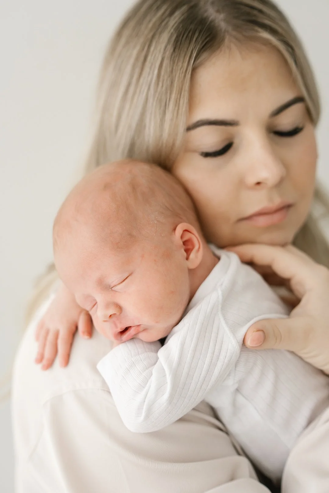 Lapsi nukkuu syliin äidin sylissä, hän on ohuissa vaatteissa ja hänen päänsä lepää äidin olkapäällä. Äiti katsoo rauhallisesti eteenpäin.