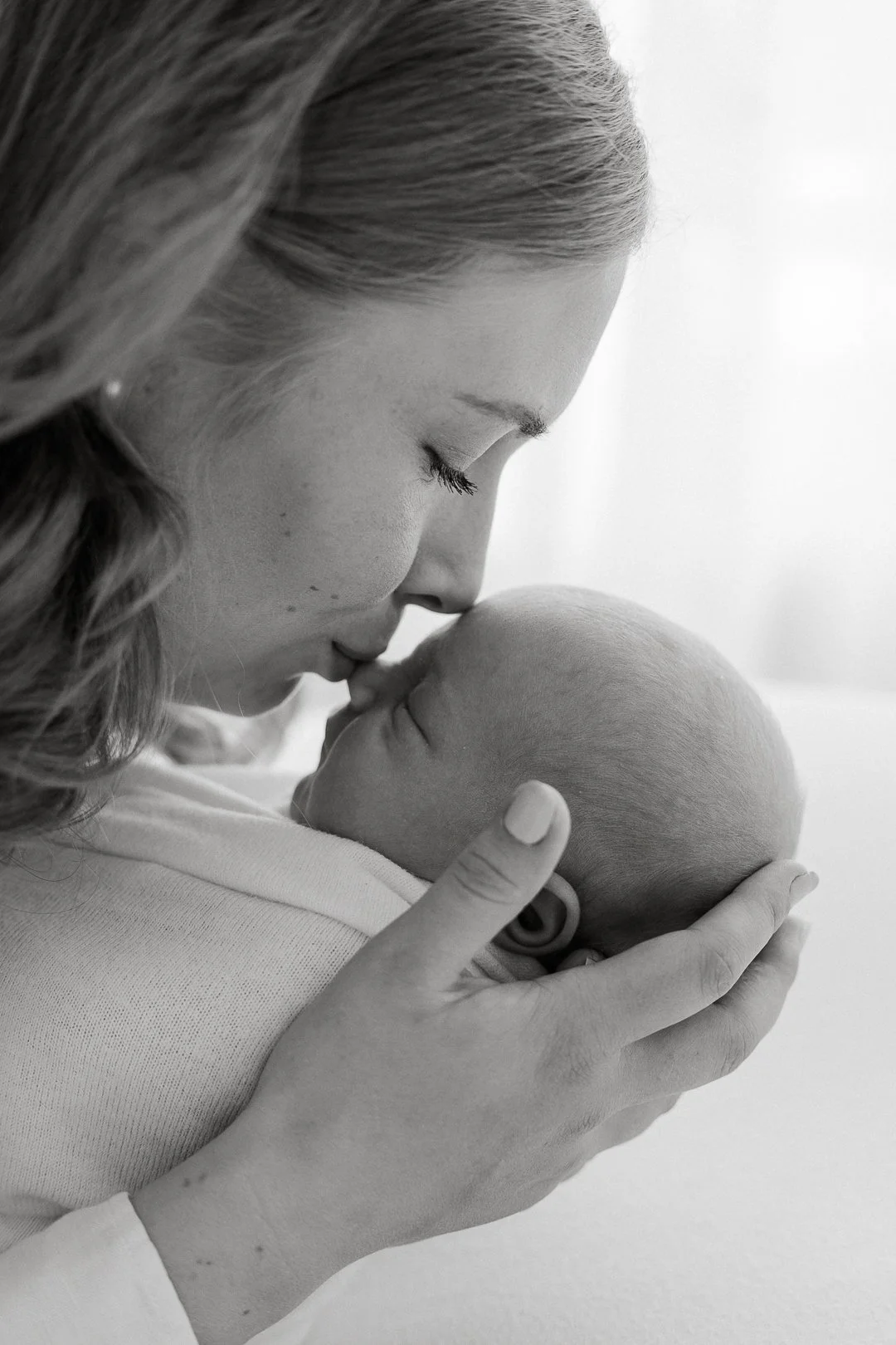 Nainen ja vauva jakavat läheisen hetkensä, nainen pitää vauvaa kasvojaan vasten ja suukottaa tätä.