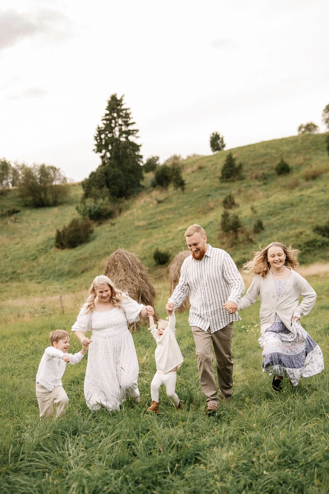 Perhe tanssii ja nauraa viljelyalueella, taustalla heinäsuovia ja puita