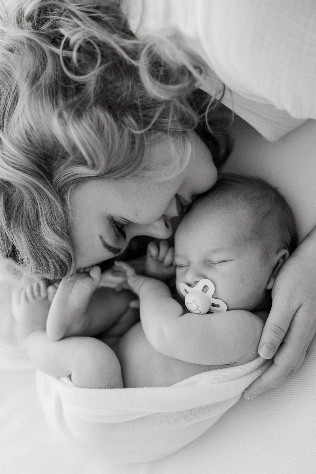 Vauva nukkuu sylissä, ja nainen koskettaa hänen hattuaan, lähekkäin samalla kun he ovat rauhallisia ja rakastavia.