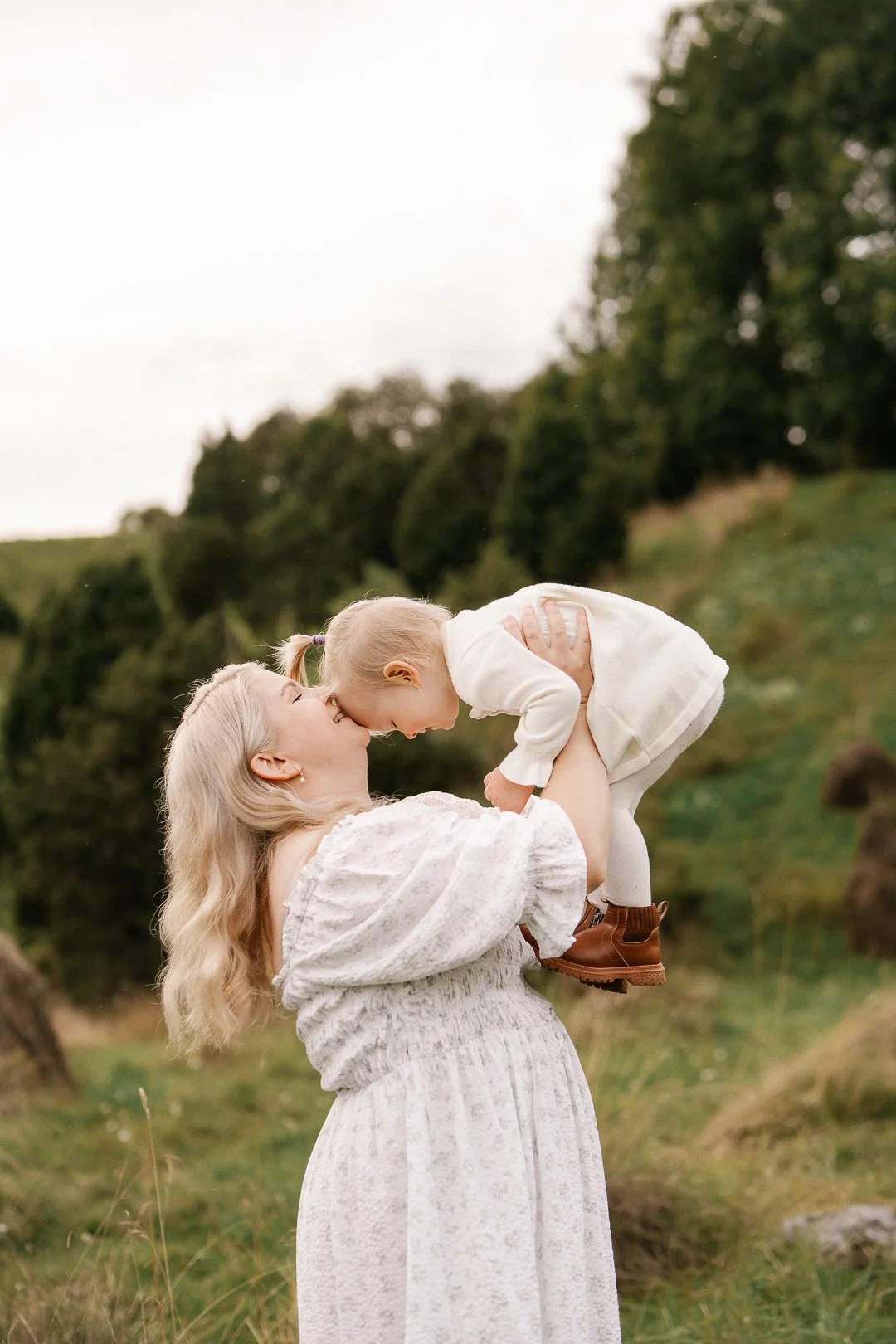 Nuori nainen ja pieni lapsi leikkivät ulkona luonnon keskellä, nainen nostaa lapsen ilmaan ja lapsi hyväilee naisen kasvoja.