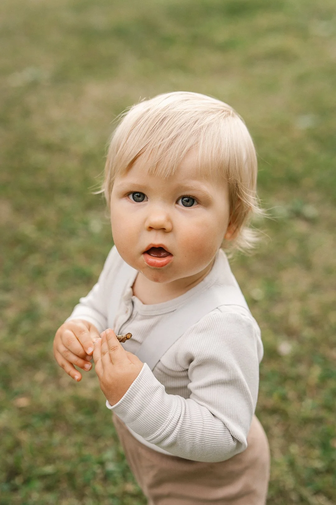 Pikku poika katsoo kameraan ulkona, taustalla ruoho ja luonto.