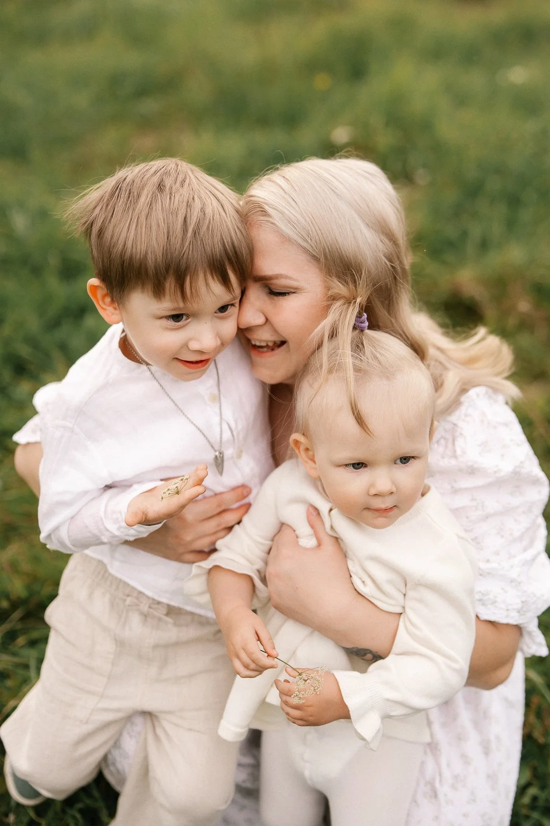 Hän on nainen ja kaksi lasta, halaavat toisiaan ulkona vihreän nurmikon keskellä.